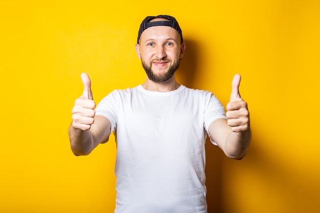 Young man friendly and happy in a white t-shirt and a baseball cap, shows a class gesture, thumb up