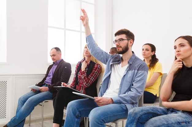 Photo young man from multiethnic audience raising hand to ask question on conference, copy space