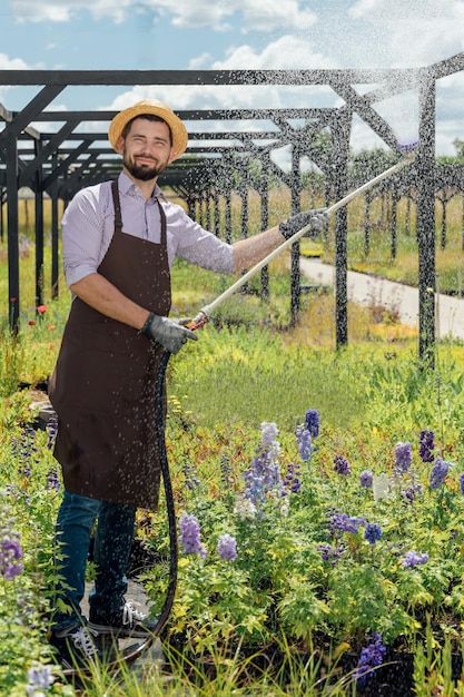 写真 若い男の庭師は、園芸用品センターでそれらに水をまくことによって植物の世話をします
