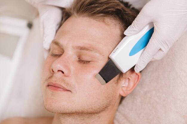 Young man getting facial skincare treatment by cosmetologist