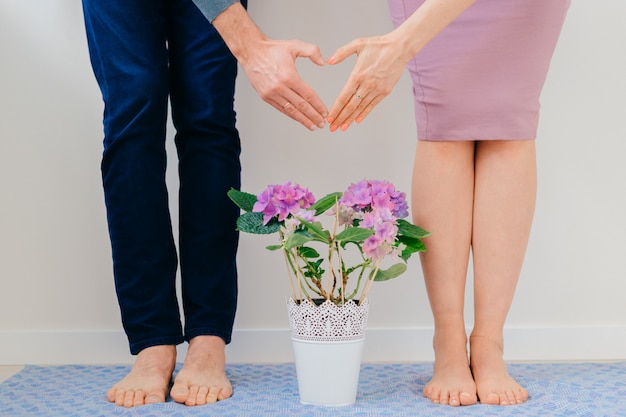 Young man and girl clasped hands and heart sign over pot of flowers. 