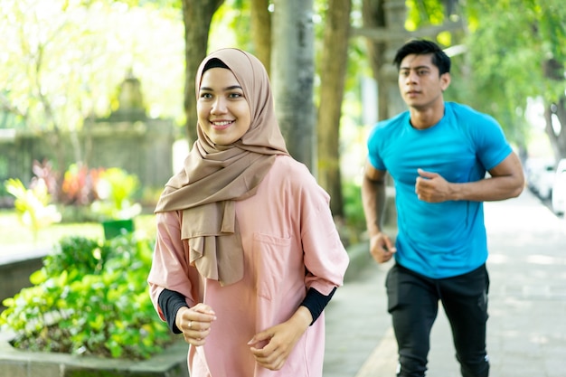 A young man and a girl in a veil doing jogging together when outdoor exercise in the park