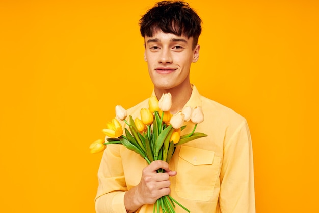 A young man give flowers wear spectacles yellow shirt yellow background unaltered