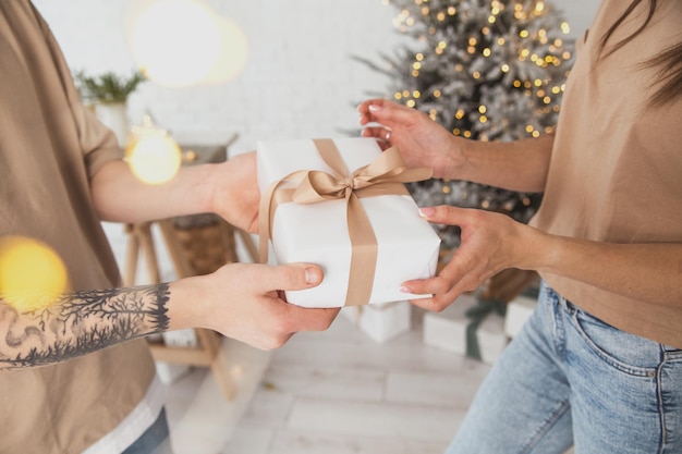 Фото Молодой человек дарит молодой женщине рождественский подарок в белом пакете с бантом