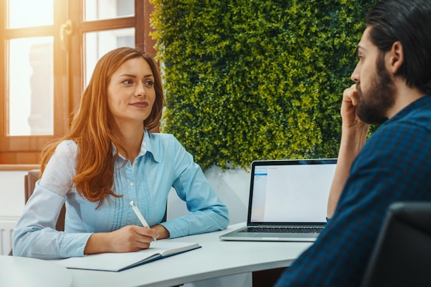 A young man gives an interview for a job, and the data is taken by a young woman.