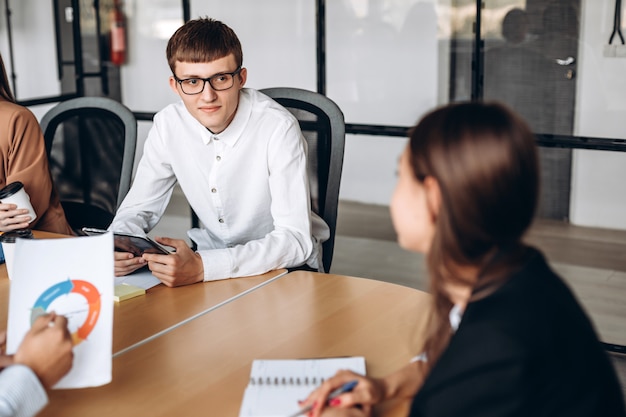 Young man in glasses at business meeting, listening carefully to his colleague