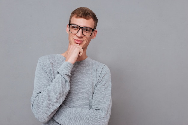 Young man in glasses, hand near the face isolated on gray