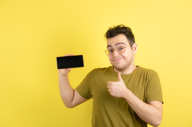  young man in glasses holding cellphone and standing. 