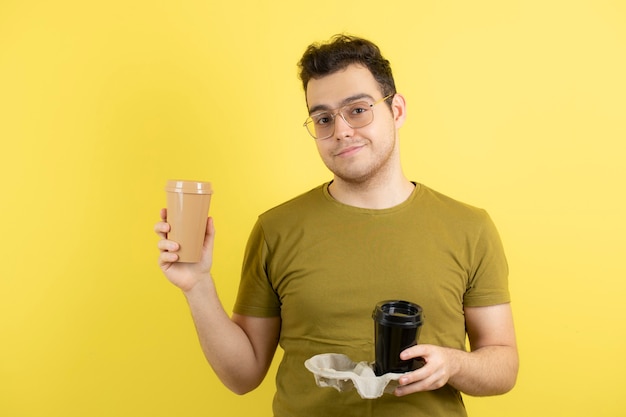  young man in glasses holding two cups of coffee. 