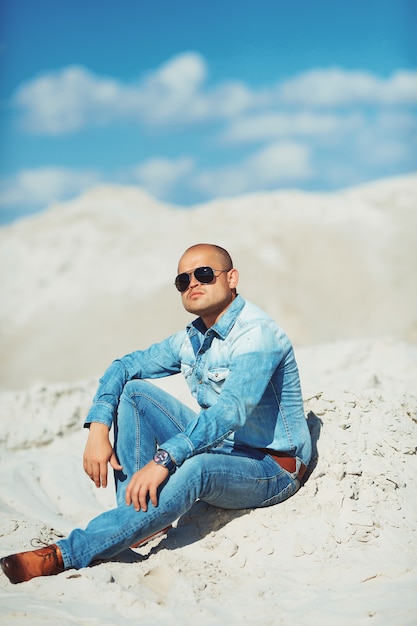 Young man in glasses lies in jeans clothes on the sand in Dubai