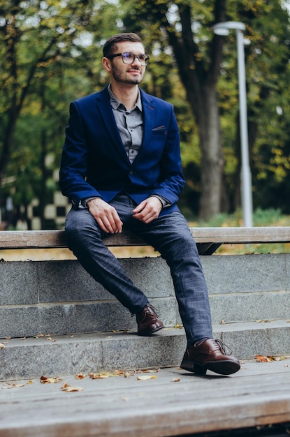 a young man in glasses sits on a bench