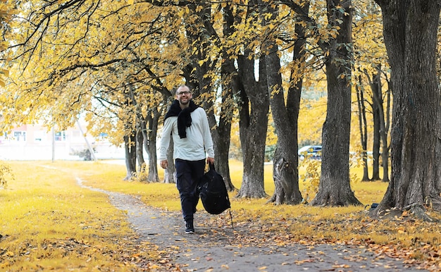 A young man in glasses walks in the park with an umbrella during the rain.