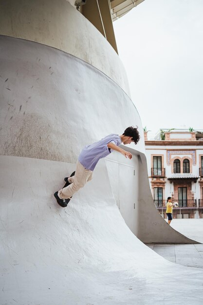 都市の彼のスケート ボードでコンクリートの傾斜ランプを上って行く若い男