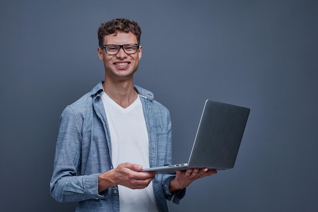 Young man on a gray background holding a laptop