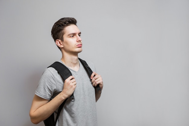 Young man in gray shirt on grey background. Student with backpack