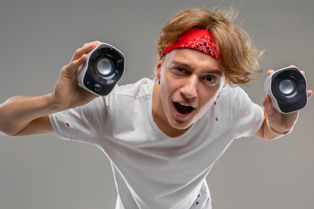 A young man in a gray shirt and a red bandana with speakers in the hands of