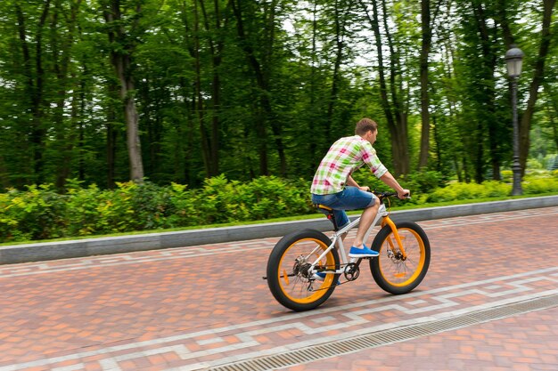 Young man in green and red plaid shirt riding a bike on a footpath in a park