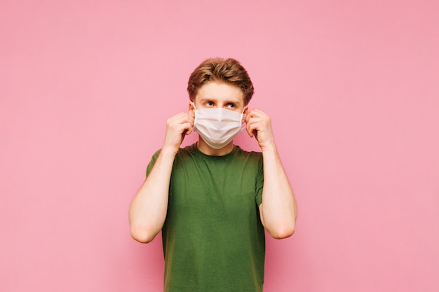 Young man in a green tshirt holding a gauze medical mask on a pink background