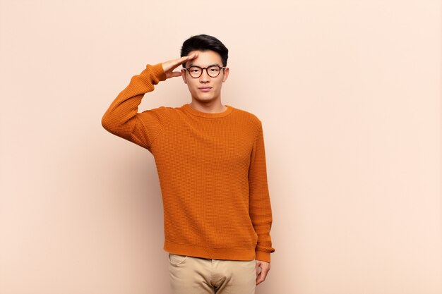 Young man greeting with a military salute in an act of honor and patriotism, showing respect against color wall