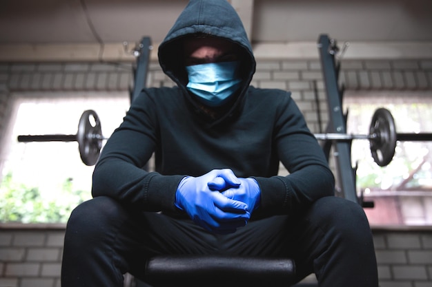 Young man in the gym with weights and protective mask and gloves for Coronavirus, Covid-19, fitness and corona concept