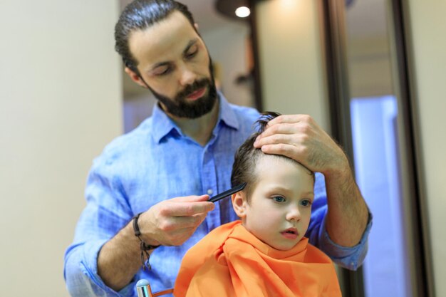 The young man the hairdresser does a hair to the boy He cuts hair with scissors