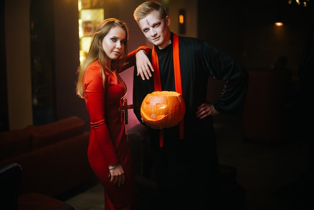 Young man in a halloween priest costume holds a carved pumpkin in his hand