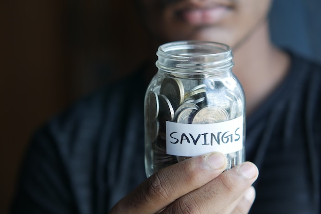 Photo young man hand hold saving coins jar