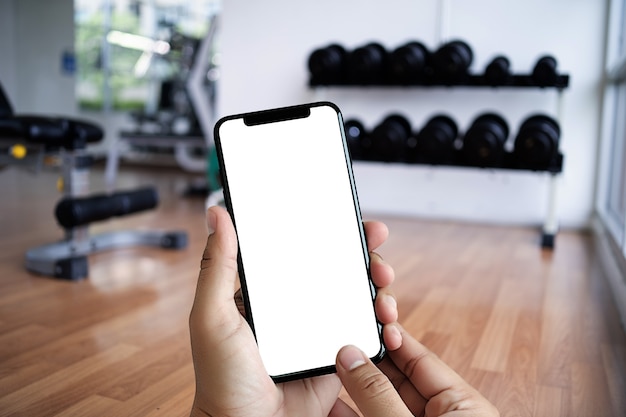 Lo smartphone della tenuta della mano del giovane in palestra al concetto di esercizio di forma fisica del telefono di forma fisica