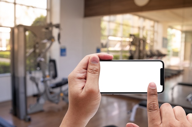 Lo smartphone della tenuta della mano del giovane in palestra al concetto di esercizio di forma fisica del telefono di forma fisica