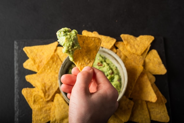 Young man hand is picking some guacamole dip with nachos chip Healthy Vegan Vegetables food