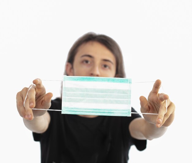 Young man handing out a protective mask on a white wall