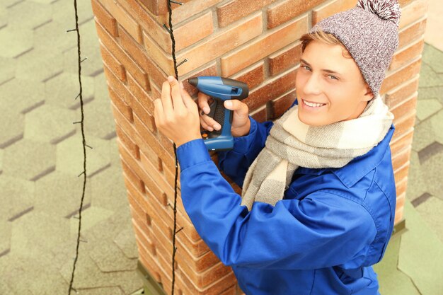 Young man hanging Christmas lights on chimney of house