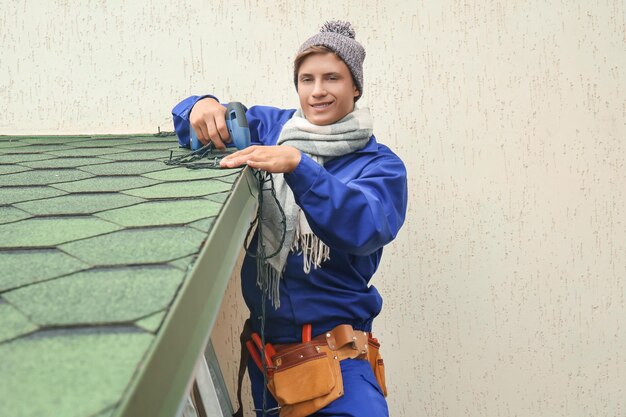 Young man hanging Christmas lights on roof of house