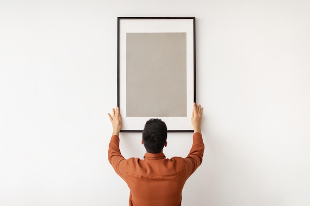 Photo young man hanging picture frame on the wall