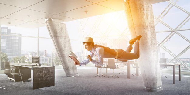 Young man in hat and casual clothes levitating in a hall. Mixed media