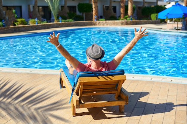 Young man in hat lying on a sun lounger at a hotel