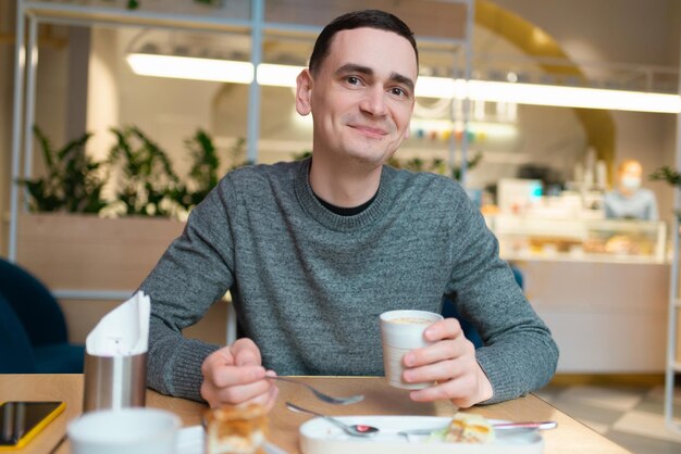 A young man having breakfast and smiling looking at the camera in a cafe