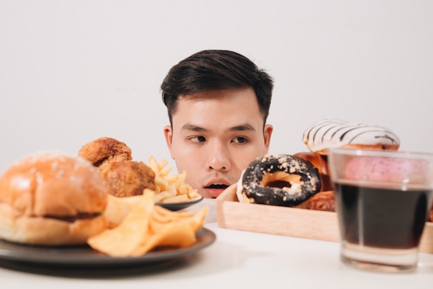 Young man having cravings for donuts, hamburger, chicken with fries instead