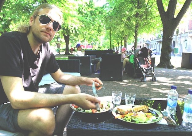 写真 街の歩道のカフェに座って食べ物を食べている若い男性