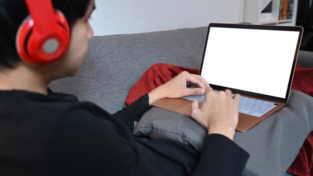 Young man in headphone using laptop on sofa