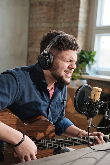 Young man in headphones singing and playing guitar during broadcasting on the radio