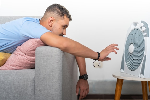 Young man in heat in front of the fan resting on the sofa