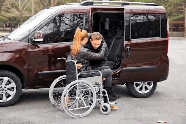 Young man helping handicapped woman to sit in wheelchair