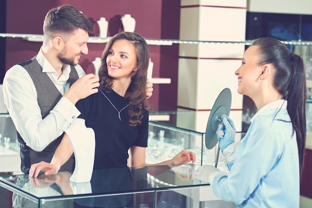 Young man helping his girlfriend with fitting necklace at the je