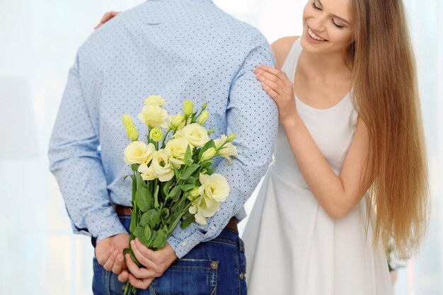 Young man hiding bouquet of flowers for his girlfriend behind back closeup