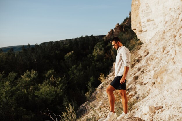 Young man hiker standing on rock from side looking to valley