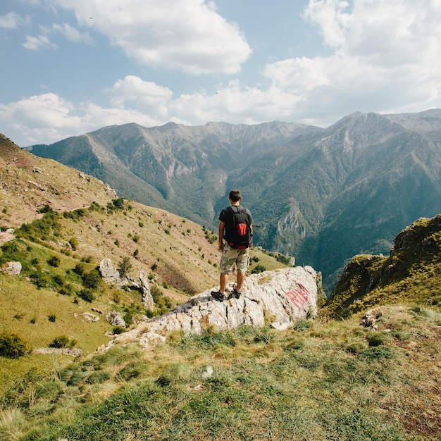 A young man hiker with a backpack is standing on a cliff with a huge depth valley in front of him