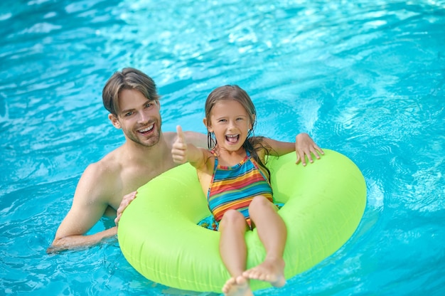 A young man and his daughter swimming in the pool and looking enjoyed