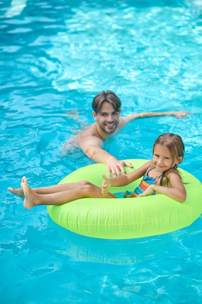 A young man and his daughter swimming in the pool and looking enjoyed