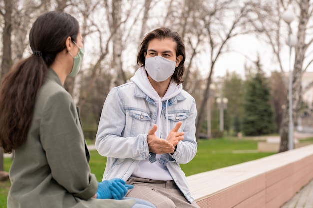 Young man and his girlfriend in protective masks and casualwear discussing something